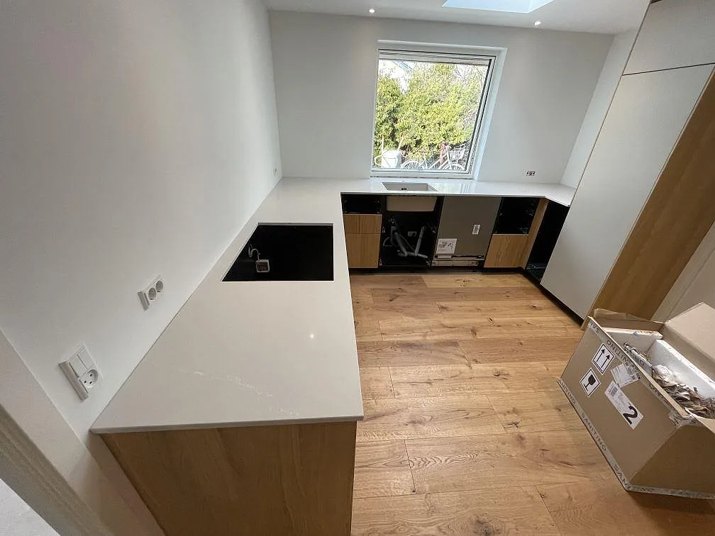 Köksbänkskiva i Silestone Desert Silver, ljust grå polerad kvartskomposit, med svart underlimmad diskho och plats för induktionshäll i en vinklad köksuppställning i Svendborg.