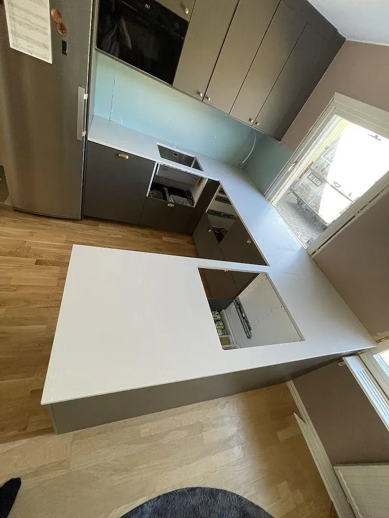 Köksbänkskiva i Silestone Desert Silver, matt gråbeige komposit med 20 mm tjocklek, monterad i L-form med köksö i ett kök under montering i Täby.