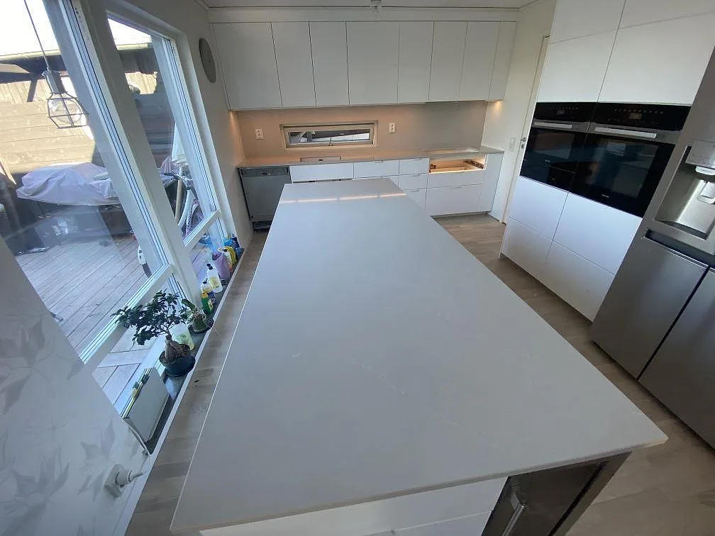 Översiktsbild av kök i Tygelsjö med stor köksö och bänkskivor i polerad Silestone Desert Silver under montering.