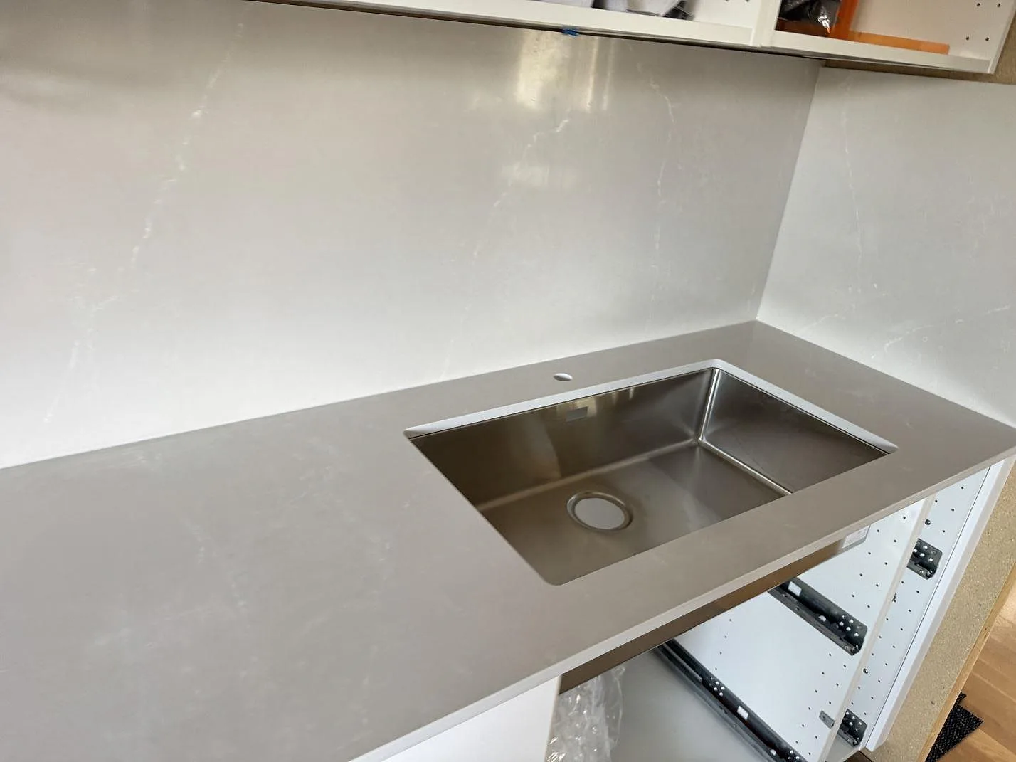 Polerad köksbänkskiva i Silestone Desert Silver med rostfri diskho och matchande stänkskydd i ett kök under montering i Vargön.