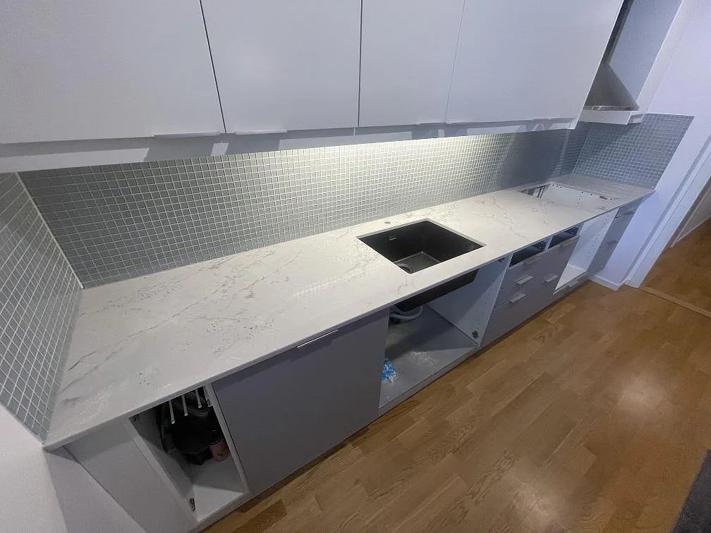 Köksbänkskiva i Silestone Eclectic Pearl, polerad, med grå ådring längs hela köksväggen och underlimmad komposithoar i ett kök i Solna.