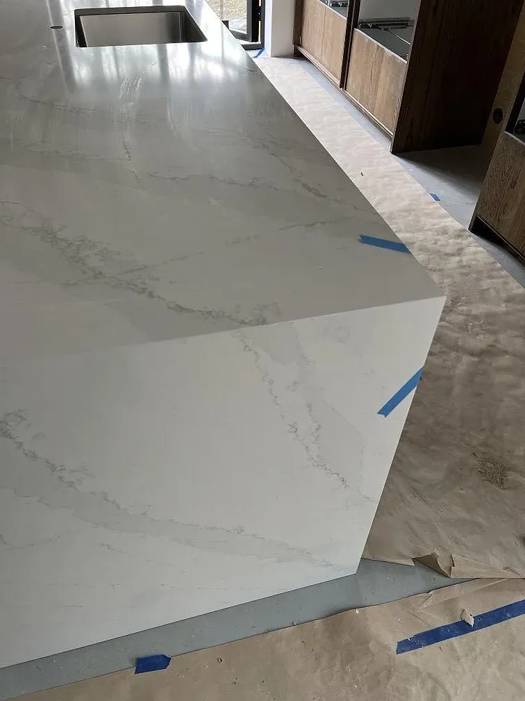 Vit köksö i Silestone Eternal Calacatta Gold, polerad komposit, med tydlig guldtonad ådring och skyddstejp vid montering i Åhus.
