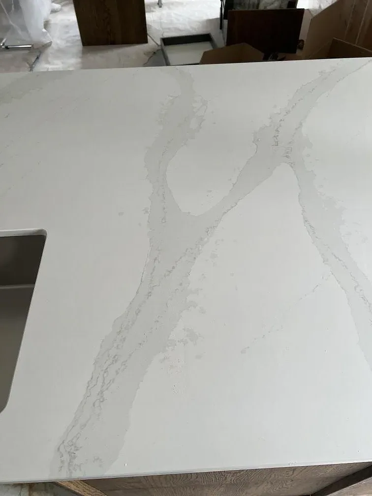 Detaljbild av vit Silestone Eternal Calacatta Gold, polerad, med mjuk ådring intill den rostfria diskhon i köket i Åhus.