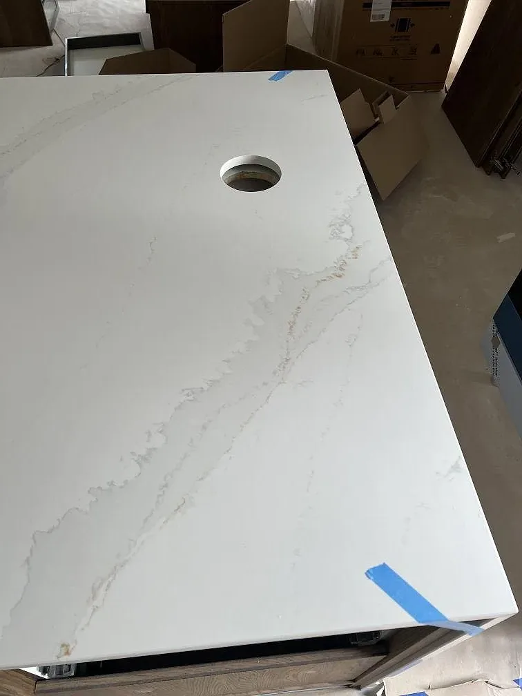 Närbild på polerad Silestone Eternal Calacatta Gold som köksbänkskiva med blandarhål, ljus ådring och blå monteringstejp i Åhus.