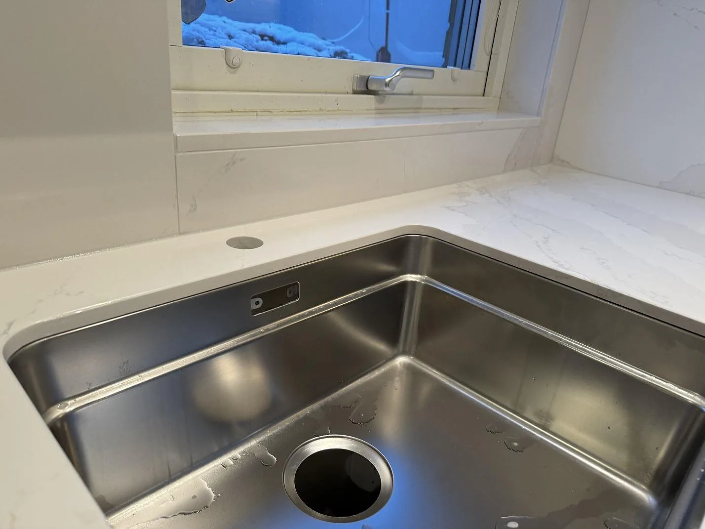 Närbild på underlimmad rostfri diskho i polerad Silestone Eternal Calacatta Gold med fönsterdel i ett kök i Bunkeflostrand.
