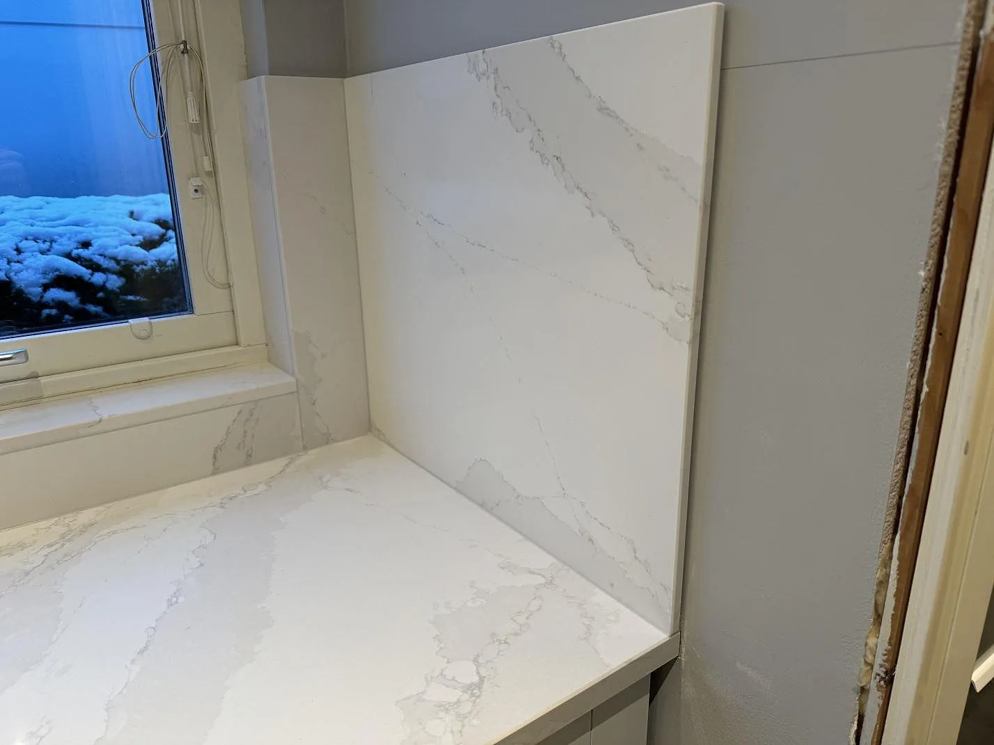 Hörndel med polerad Silestone Eternal Calacatta Gold, fönsterdel och högt stänkskydd under montering i Bunkeflostrand.