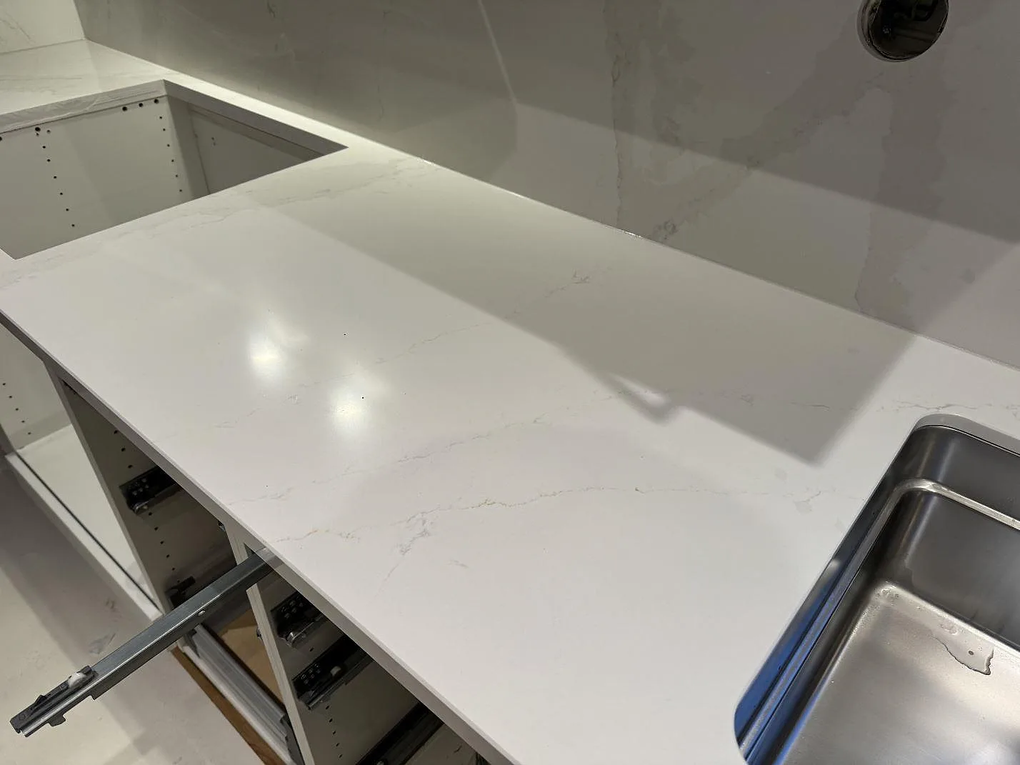 Polerad Silestone Eternal Calacatta Gold-bänkskiva med hällöppning, diskho och öppna köksstommar under montering i Bunkeflostrand.