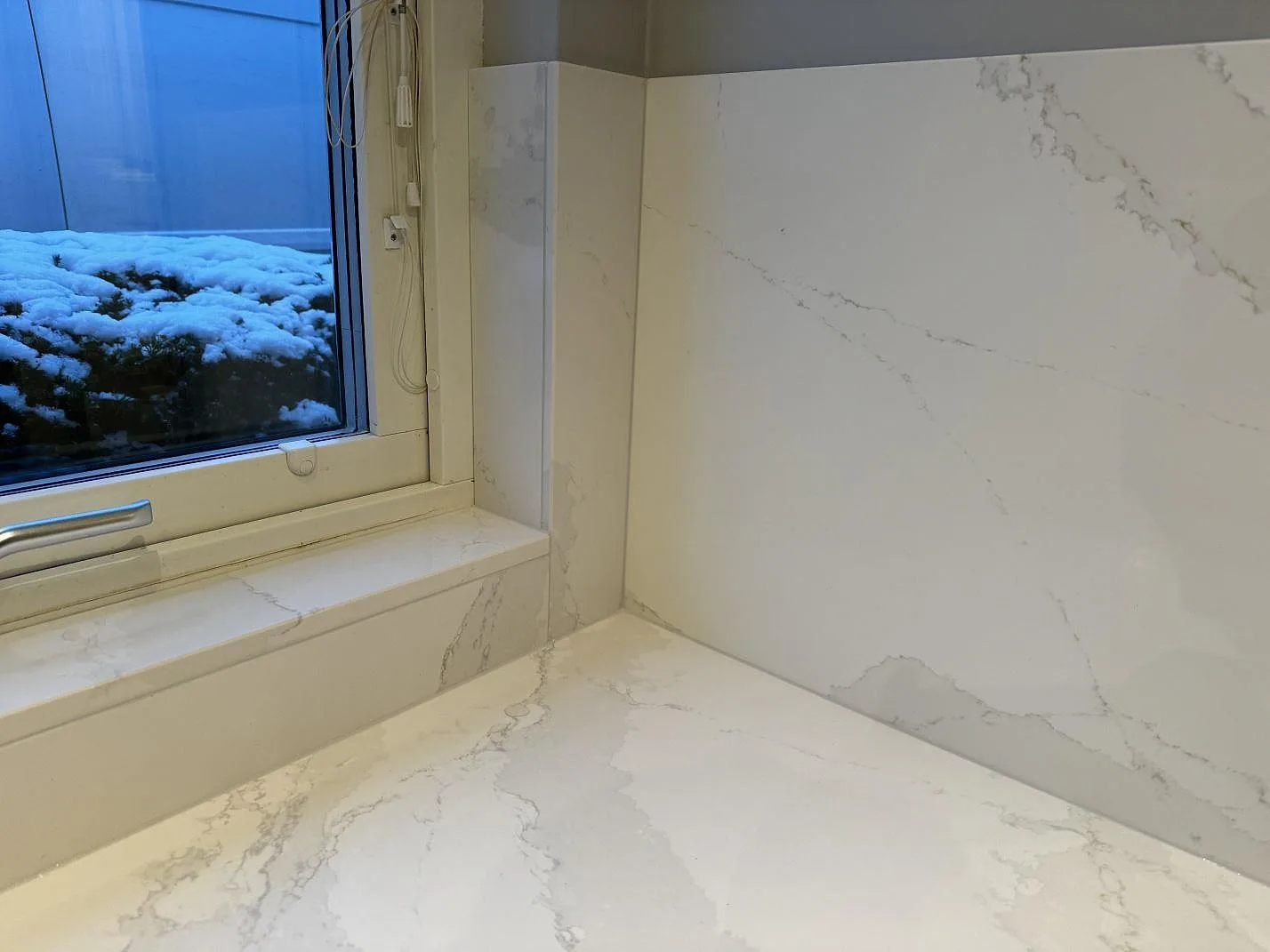 Detalj av fönsterbänk, bänkskiva och stänkskydd i polerad Silestone Eternal Calacatta Gold vid ett köksfönster i Bunkeflostrand.