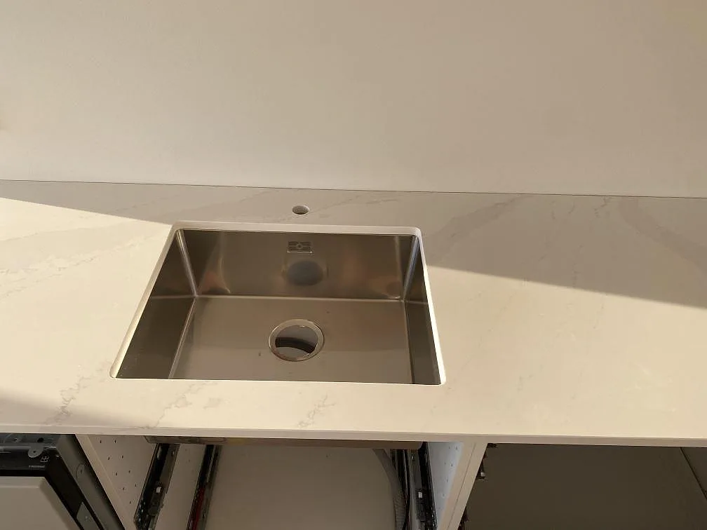 Underlimmad rostfri diskho i en polerad köksbänkskiva av Silestone Eternal Calacatta Gold i ett kök i Halmstad.