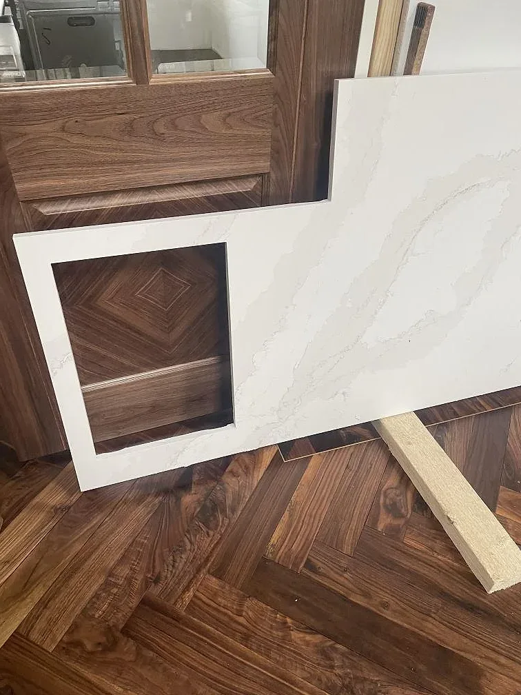 Köksö i Silestone Eternal Calacatta Gold med urtag i skivan, mot valnötsinredning och fiskbensparkett i ett kök i Hornbæk.