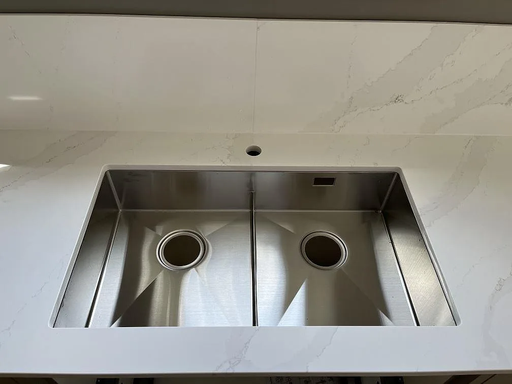 Underlimmad dubbel diskho i rostfritt stål i köksbänkskiva av polerad Silestone Eternal Calacatta Gold i ett kök i Löddeköpinge.