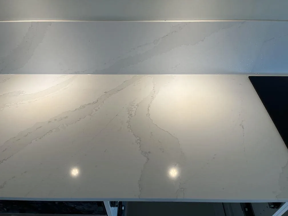 Svart induktionshäll infälld i den polerade köksbänkskivan av Silestone Eternal Calacatta Gold i ett kök i Malmö.
