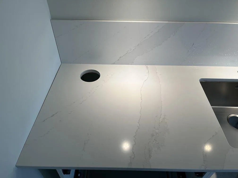 Detalj av den underlimmade rostfria diskhon och den polerade Calacatta Gold-ytan med kranhål i ett kök i Malmö.