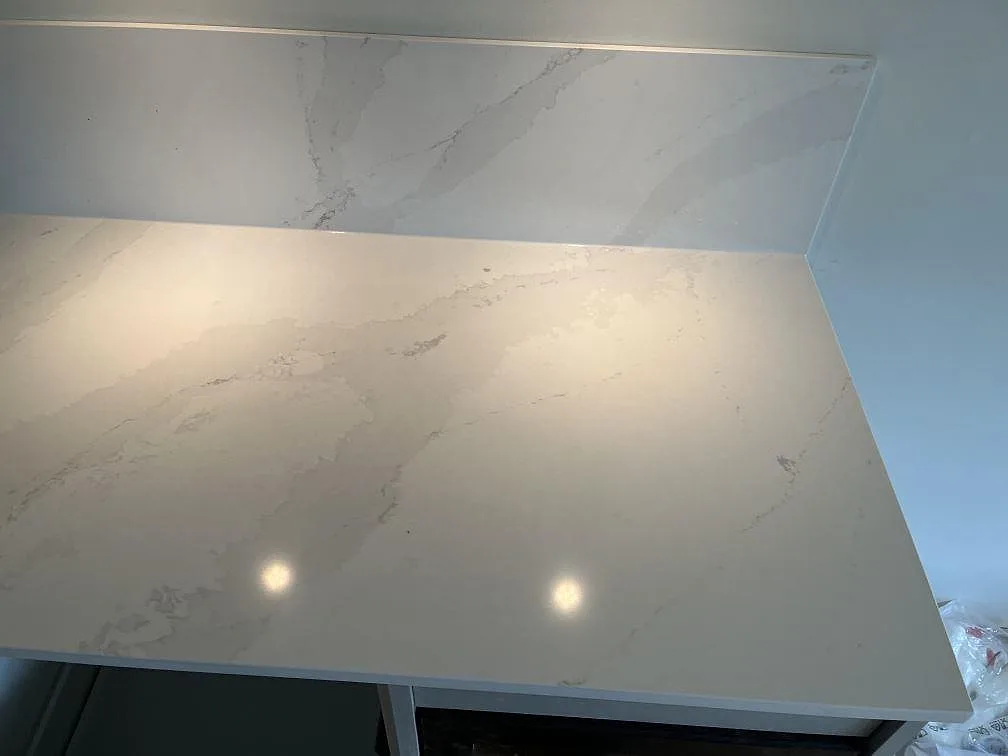 Polerad köksbänkskiva i Silestone Eternal Calacatta Gold med mjuk grå och guldaktig ådring och uppvikt stänkskydd i ett kök i Malmö.