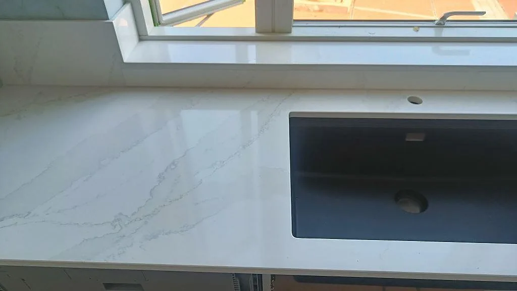 Närbild på polerad köksbänkskiva i Silestone Eternal Calacatta Gold med mörk diskho och blandarhål vid fönster i Malmö.