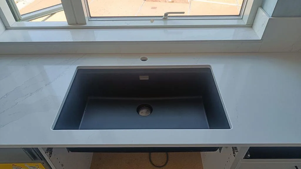 Mörk underlimmad diskho monterad under polerad Silestone Eternal Calacatta Gold i ett vitt kök i Malmö.