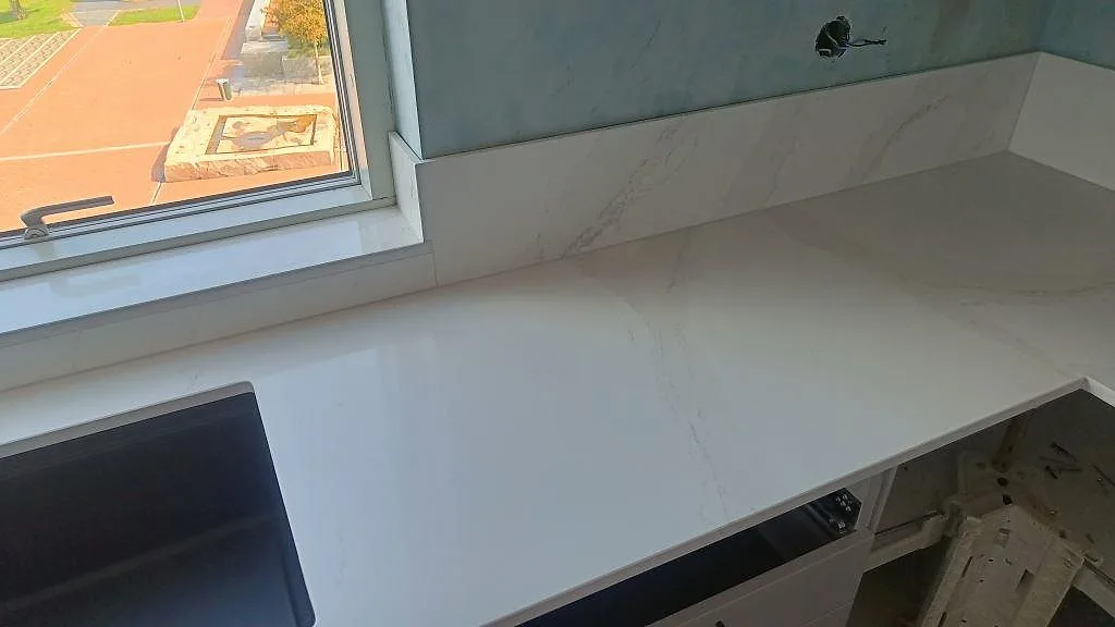 Hörnparti med köksbänkskiva och stänkskydd i polerad Silestone Eternal Calacatta Gold under montering i Malmö.