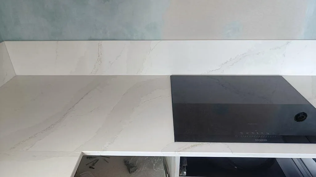 Svart induktionshäll i polerad köksbänkskiva av Silestone Eternal Calacatta Gold med matchande stänkskydd i Malmö.