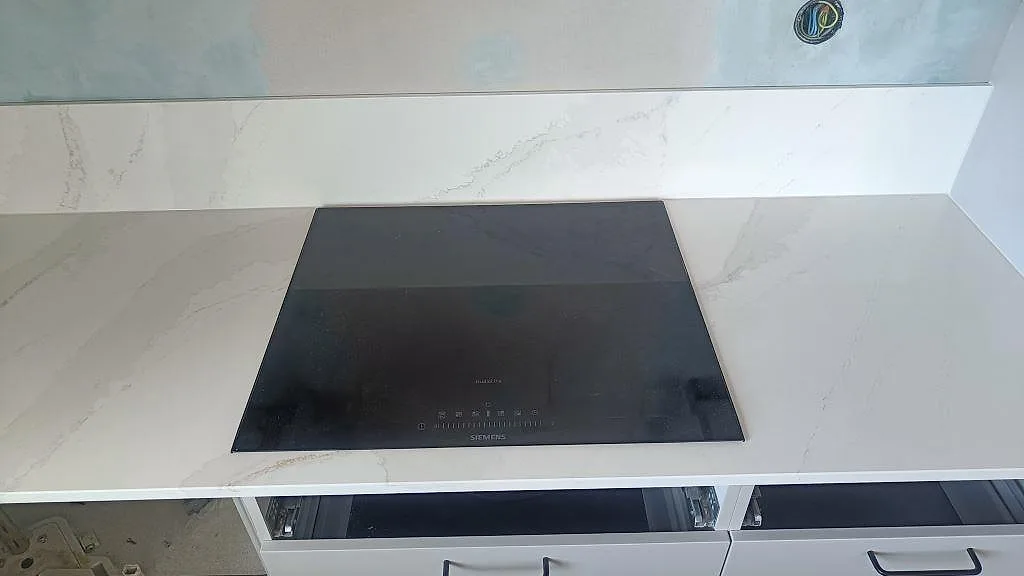 Hällsida med svart induktionshäll och vit polerad Silestone Eternal Calacatta Gold som köksbänkskiva i Malmö.