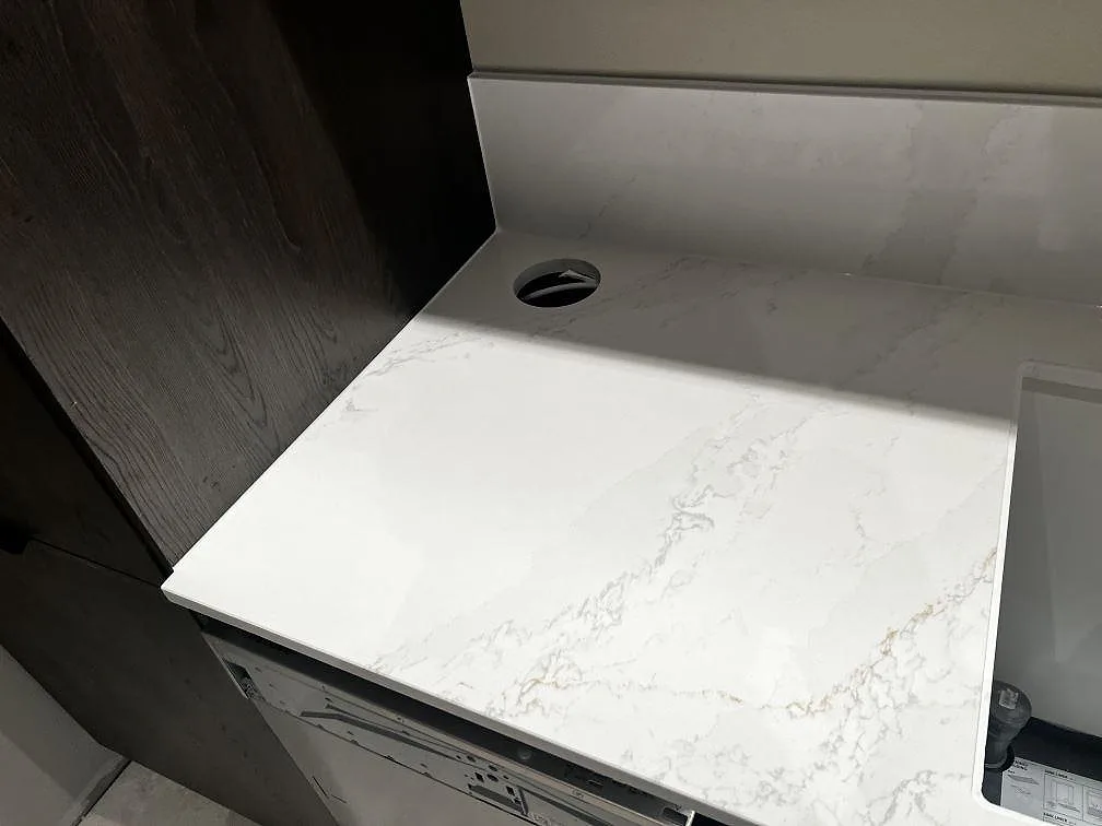 Detalj av polerad Silestone Eternal Calacatta Gold vid rund håltagning, träinredning och öppen köksstomme i Malmö.