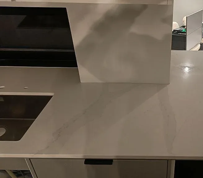 Köksbänkskiva i Silestone Eternal Calacatta Gold, polerad vit kvartskomposit med grå och guldfärgad ådring, över köksö och bänk med diskho och häll i ett kök i Mörrum.