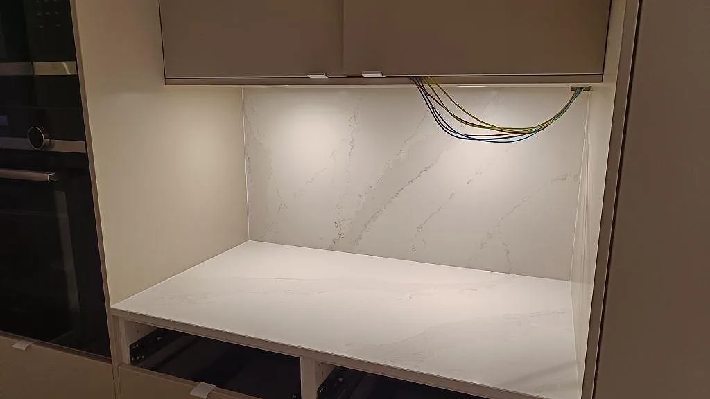 Ljus köksbänkskiva och stänkvägg i polerad Silestone Eternal Calacatta Gold under väggskåp i Onsala.