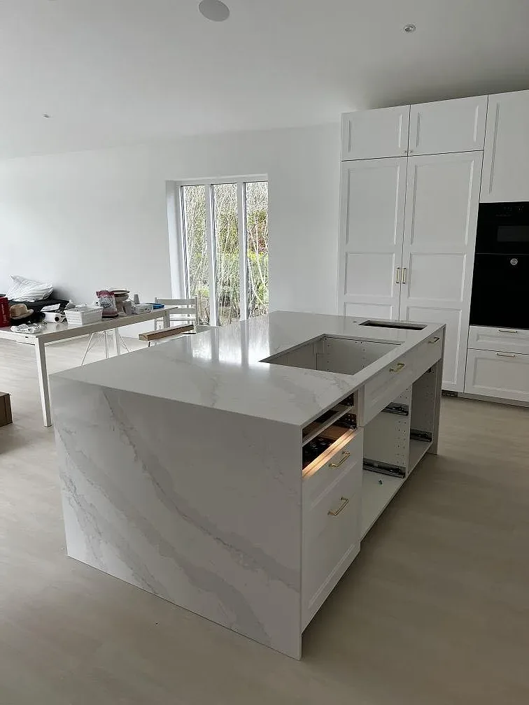 Kök under montering med köksö i polerad Silestone Eternal Calacatta Gold och vita luckor i Simrishamn.