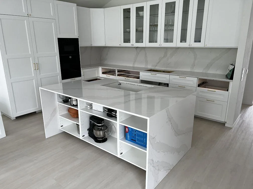 Köksbänkskiva i vit Silestone Eternal Calacatta Gold, polerad, med vattenfallsö och stänkvägg i ett vitt kök i Simrishamn.