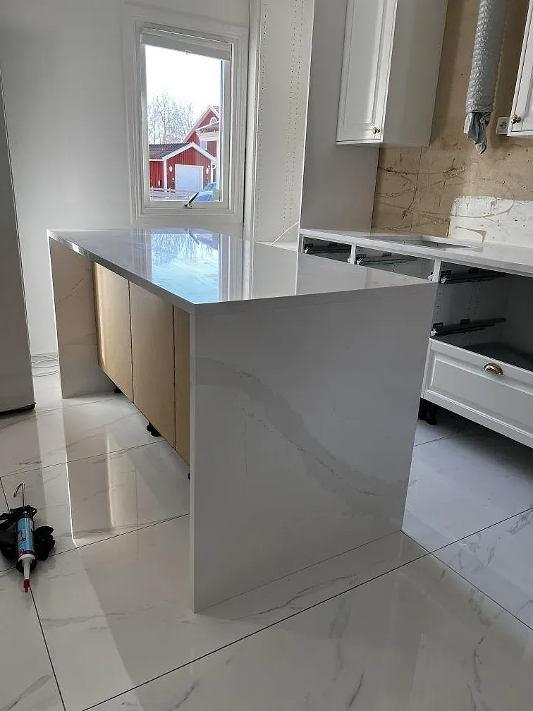 Köksö i Silestone Eternal Calacatta Gold med nedfälld gavel mot fönster i ett kök i Skövde.