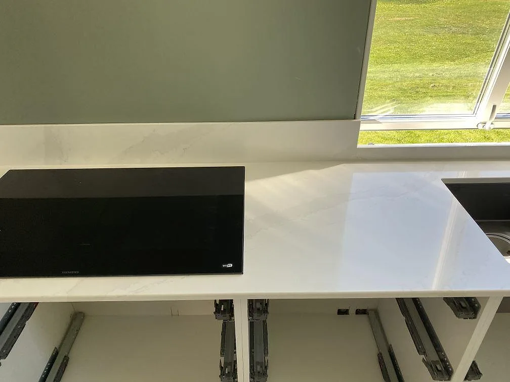 Köksbänk i Silestone Eternal Calacatta Gold med öppna lådfronter under montering och svart mikrovågsugn i ett kök i Skövde.