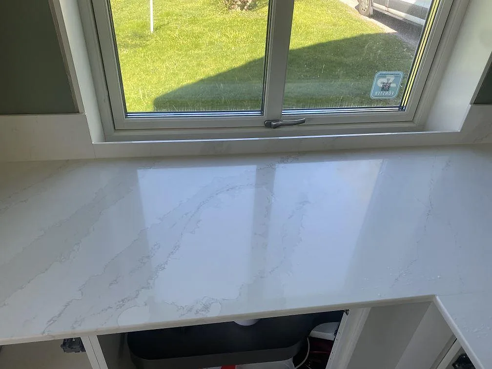 Polerad köksbänk i vit Silestone Eternal Calacatta Gold med fönsterbänk i samma sten, fotad under montering med öppna stommar i ett kök i Skövde.