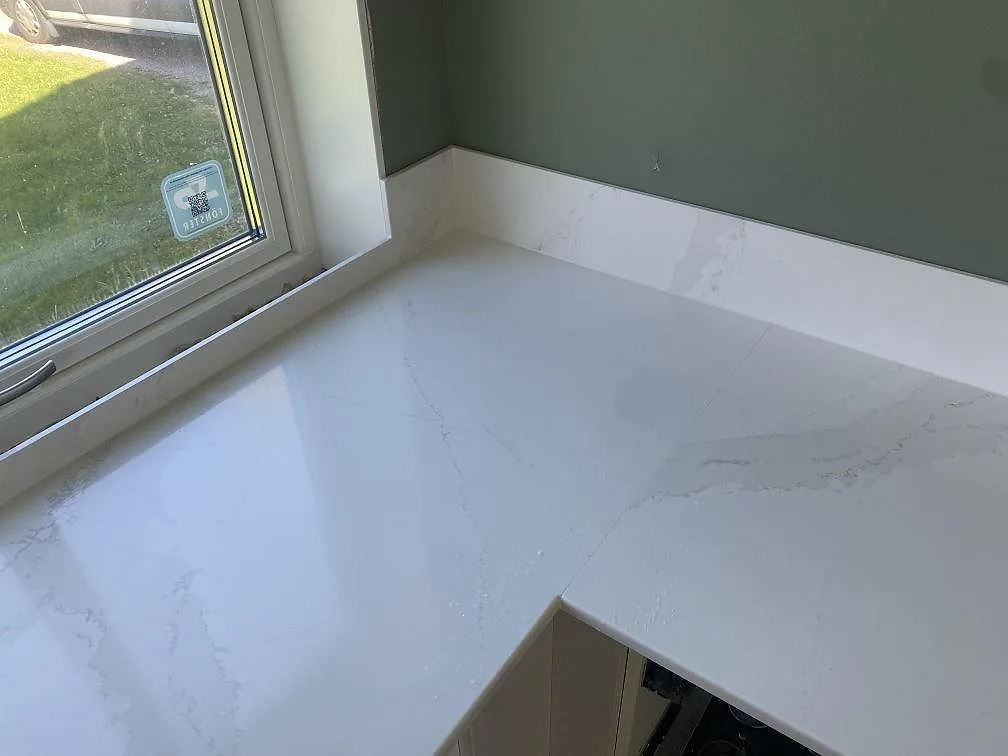Vit Silestone Eternal Calacatta Gold köksbänk i L-format med tydlig grå ådring och fönsterbänk i samma sten, fotad under montering i ett kök i Skövde.