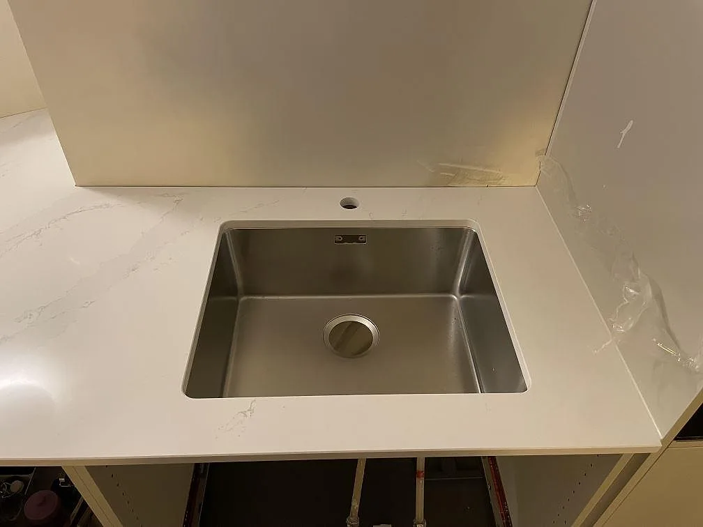 Underlimmad rostfri diskho i en köksbänkskiva av vit Silestone Eternal Calacatta Gold i Stockholm.