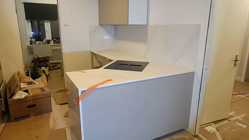 Polerad Silestone Eternal Calacatta Gold som köksbänkskiva och stänkskydd med induktionshäll och orange skyddstejp i Vellinge.