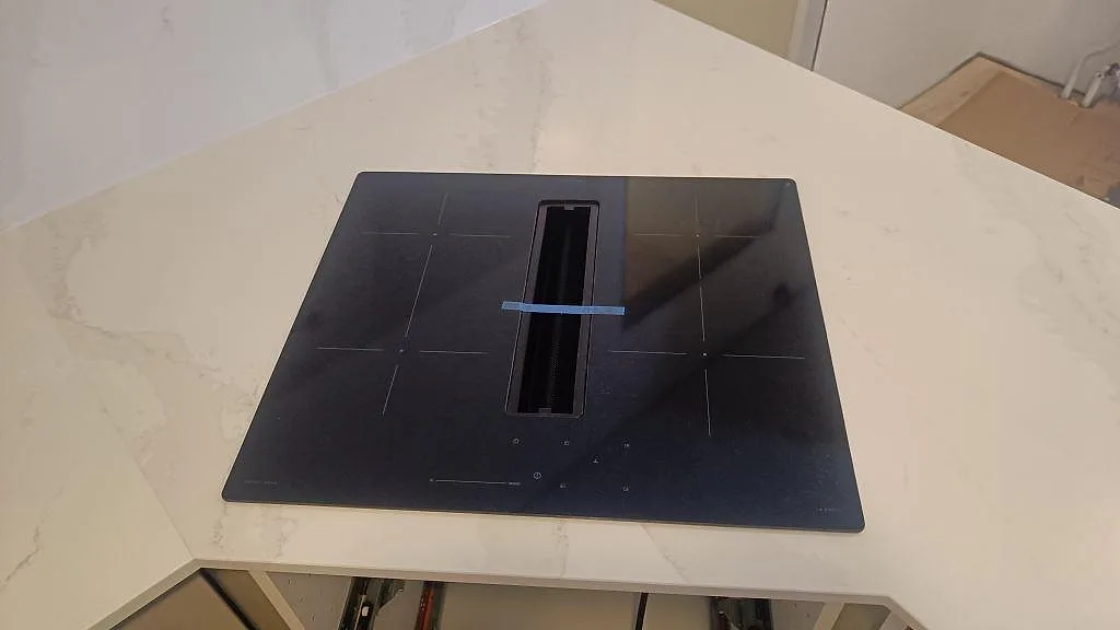 Närbild på induktionshäll i polerad Silestone Eternal Calacatta Gold med vit och guldgrå ådring i ett kök i Vellinge.