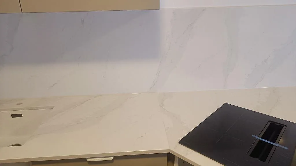 Köksbänk i polerad Silestone Eternal Calacatta Gold med diskho, induktionshäll och 12 mm stänkskydd under montering i Vellinge.