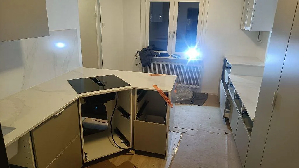 Köksbänkskiva i polerad Silestone Eternal Calacatta Gold med köksö, induktionshäll och öppna stommar under montering i Vellinge.