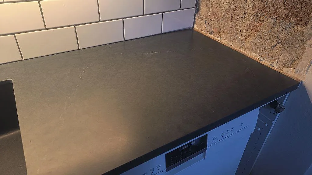 Detalj av mörk köksbänkskiva i Silestone Eternal Charcoal Soapstone, matt, intill vitt kakel och rå stenaccent i Göteborg.