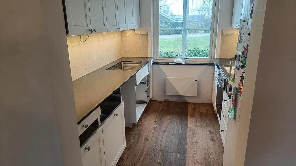 Köksbänkskiva i polerad Silestone Eternal Charcoal Soapstone, mörk kvartskomposit, monterad i ett vitt kök i Södra Sandby.