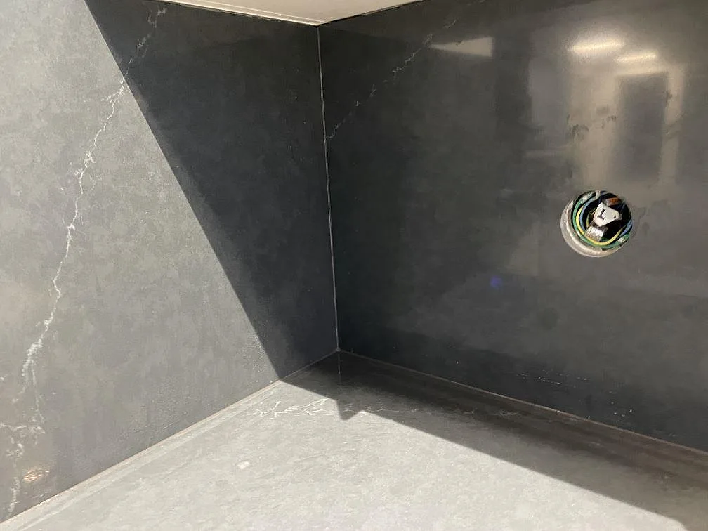 Helhetsvy av kök i Trollhättan med lång polerad Silestone Eternal Charcoal Soapstone köksbänkskiva, mörkt stänkskydd, grå skåp och rostfri diskho.