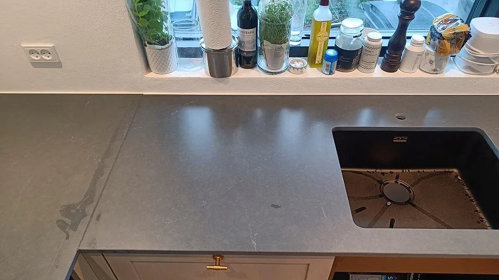 Mörk kompositbänkskiva i Silestone Eternal Charcoal Soapstone med underlimmad svart kompositdiskho under fönstret i ett kök i Vedbæk.