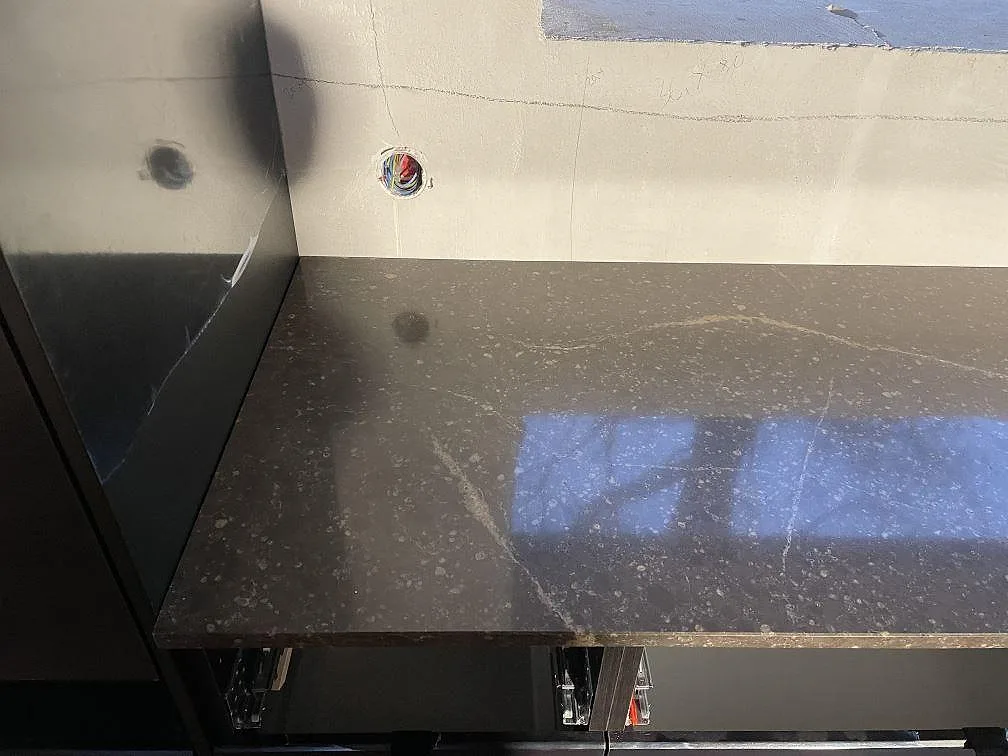Brun köksbänkskiva i polerad Silestone Eternal Emperador mot obeklädd vägg med synligt eluttag under montering i Urshult.