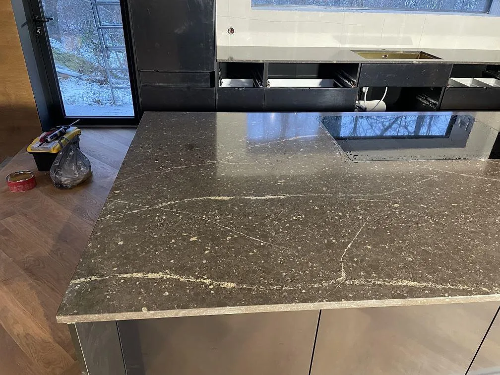 Köksö i polerad Silestone Eternal Emperador med ljus ådring, eye-level vy mot fönster i ett kök i Urshult.