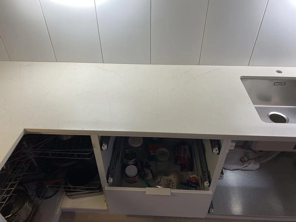Polerad kompositbänkskiva i Silestone Eternal Marfil med rostfri diskho och öppna underskåp under montering i Lomma.