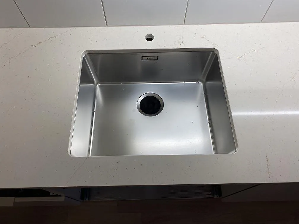 Detalj av rostfri diskho i polerad Silestone Eternal Marfil, ljus kompositbänkskiva i ett kök i Lomma.
