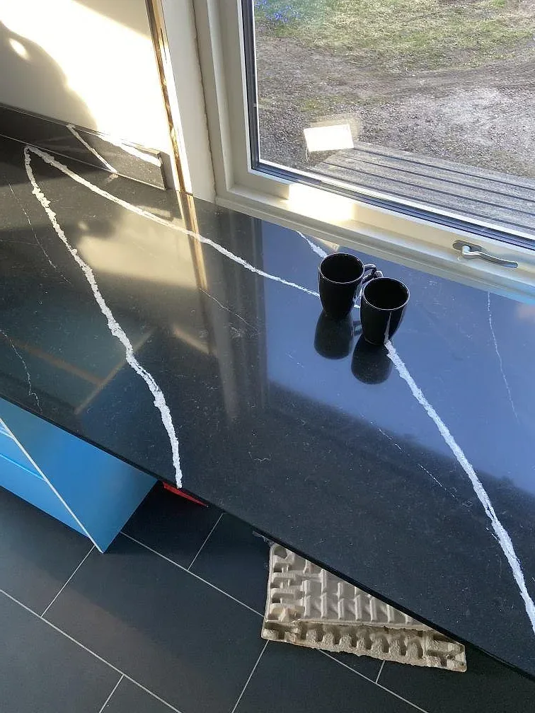 Köksbänkskiva och fönsterbänk i svart Silestone Eternal Marquina med vit ådring vid ett fönster i ett kök i Eslöv.