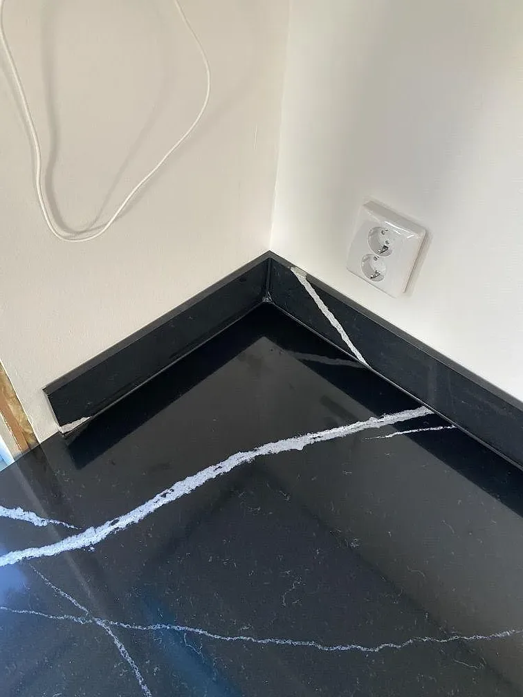 Hörndetalj av köksbänkskiva i svart Silestone Eternal Marquina med uppvikt stänkkant och vit ådring i ett kök i Eslöv.
