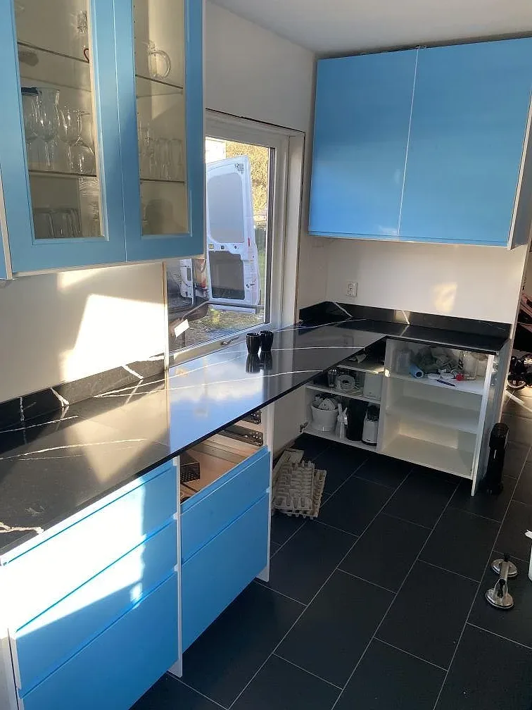 Köksparti i Eslöv med köksbänkskiva i svart Silestone Eternal Marquina, blå skåp och öppet bänkskåp under monteringen.