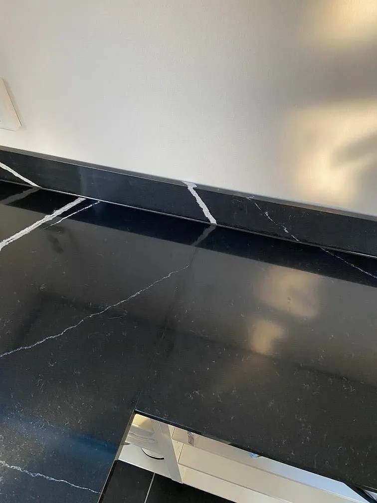 Närbild på polerad kant och stänkkant i svart Silestone Eternal Marquina med spegelblank yta och vit marmorlik ådring i ett kök i Eslöv.