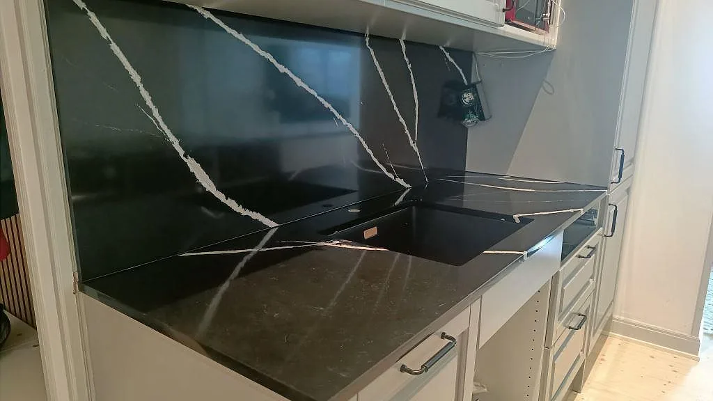Väggbänk i polerad Silestone Eternal Marquina med heltäckande stänkvägg i samma svarta sten och vita lådfronter i ett kök i Malmö.